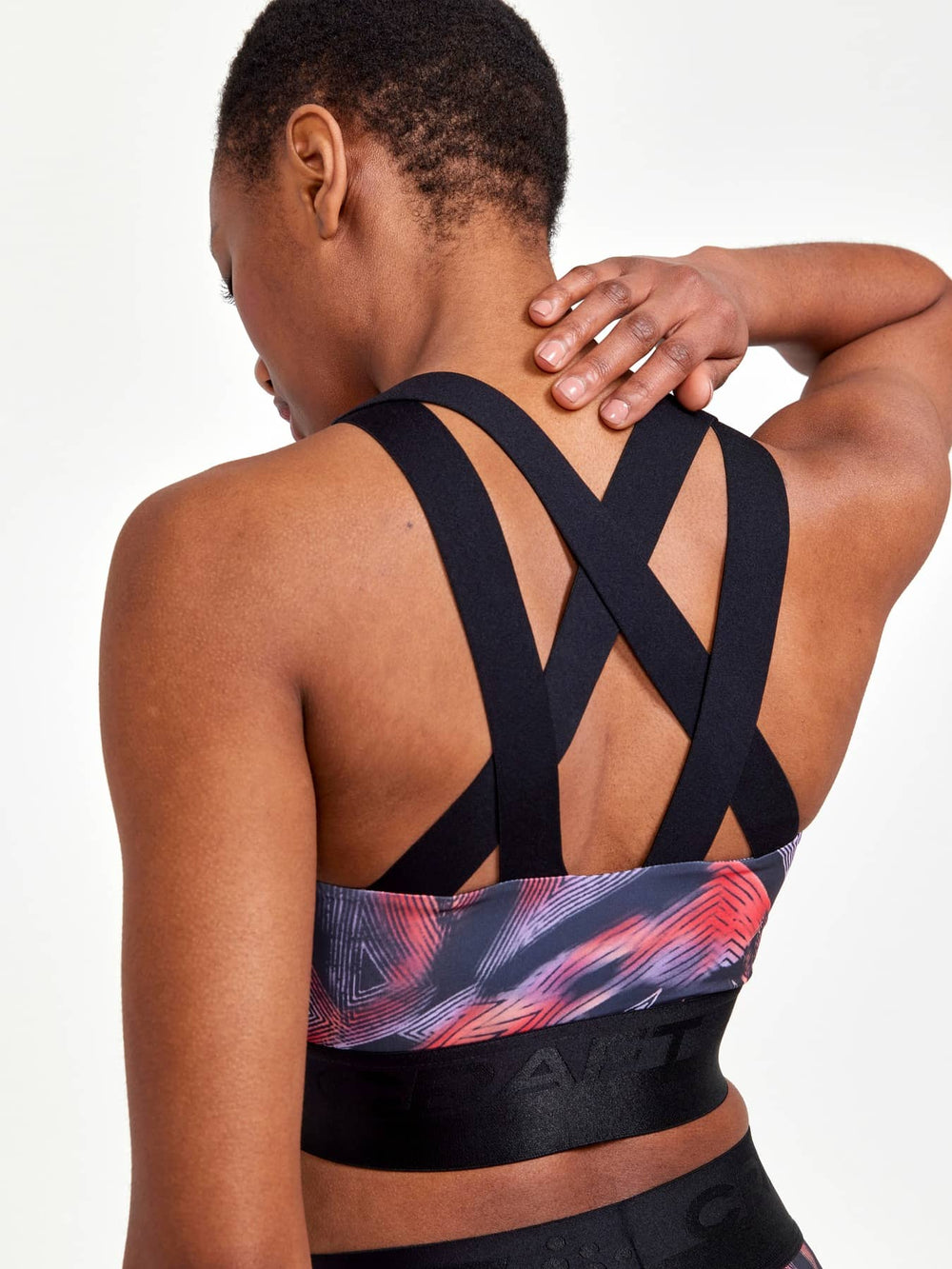 Person wearing a black sports bra with colorful design on a plain background