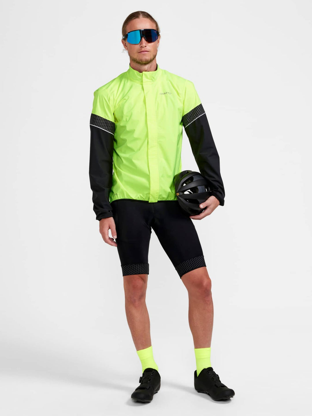 Person wearing a bright yellow cycling jacket and black shorts with a helmet on a white background