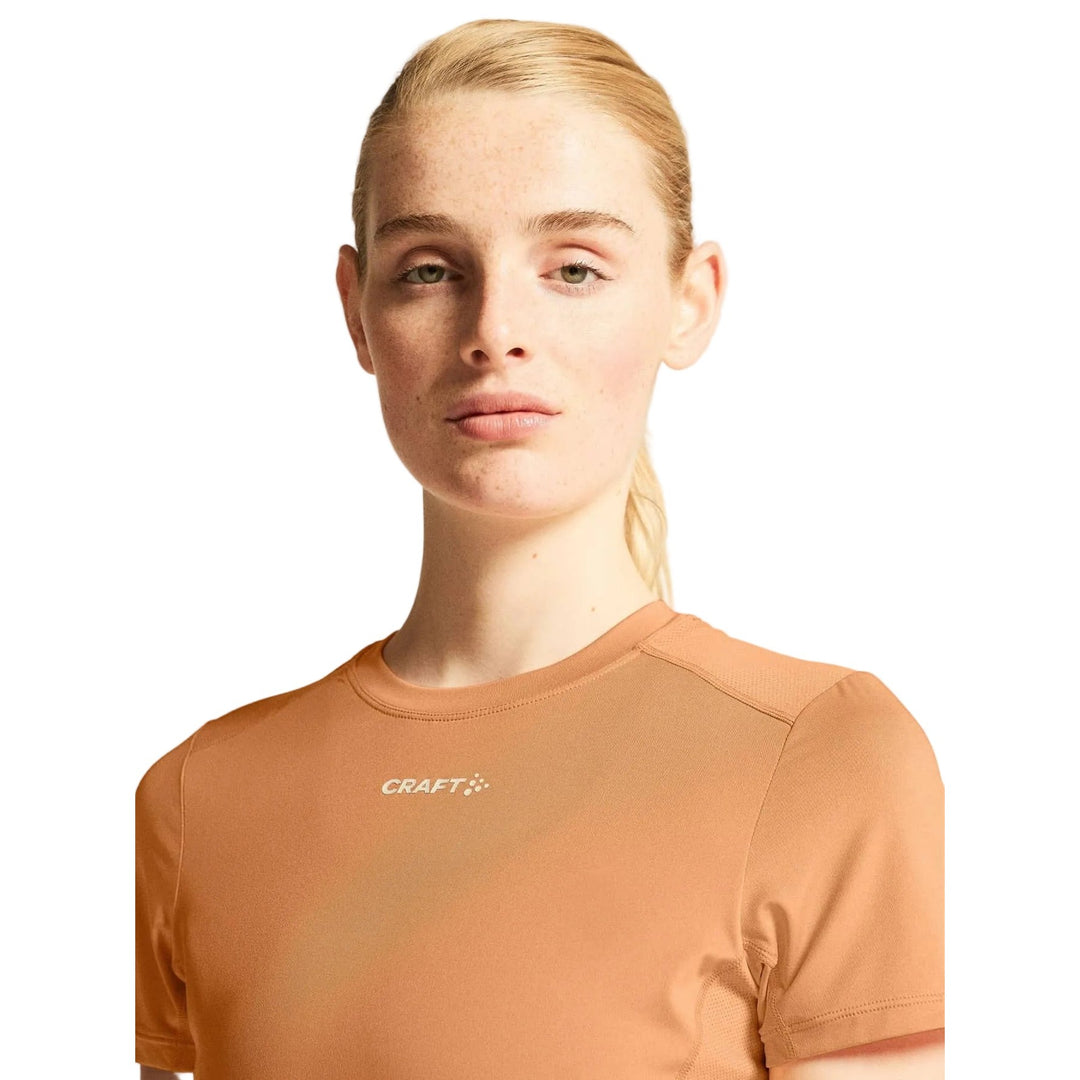 Female model wearing Craft ADV Essence SS Tee 2 in Apricot, lightweight training t-shirt designed for running, fitness, and active lifestyles.