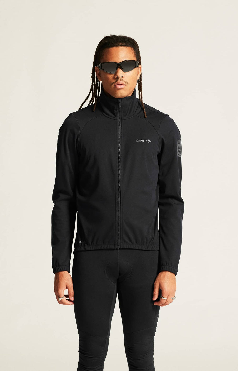 Person wearing a black jacket with a brand logo on a plain background