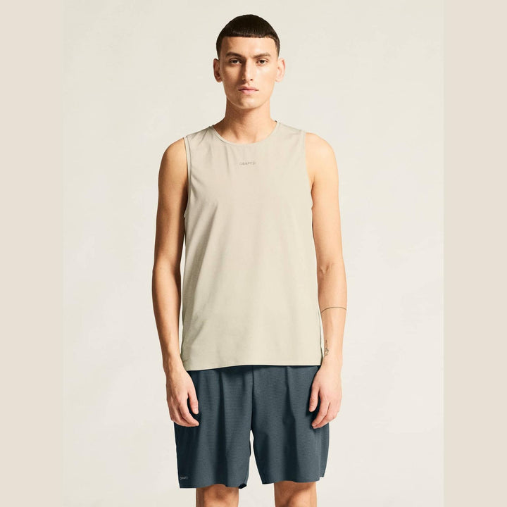 Man wearing a beige sleeveless shirt and dark shorts on a plain background