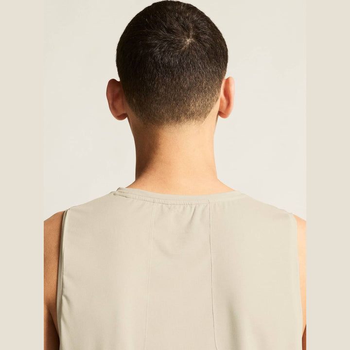 Back view of a person wearing a beige sleeveless shirt against a plain background