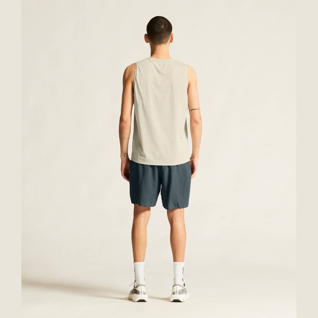 Person wearing a beige tank top and dark shorts on a plain background