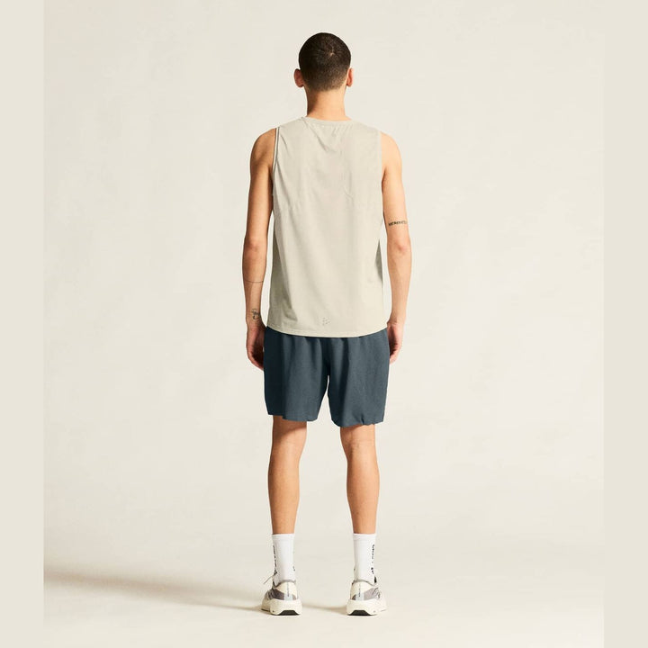 Person wearing a beige tank top and dark shorts on a plain background