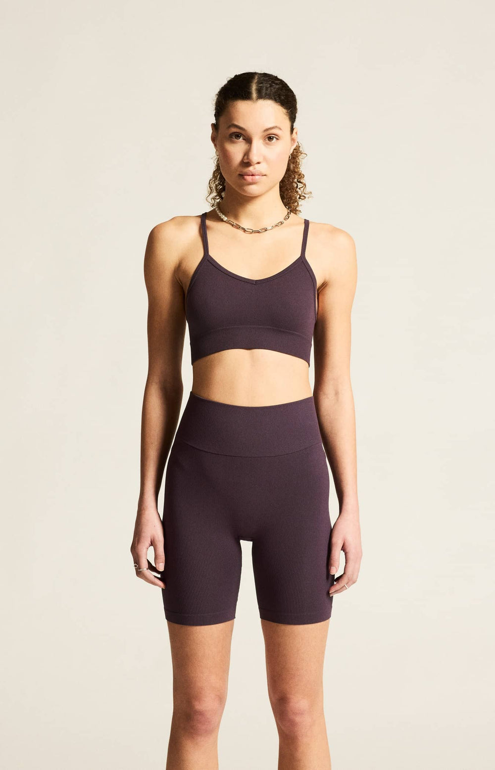 Woman wearing a dark purple sports bra and high-waisted shorts on a beige background