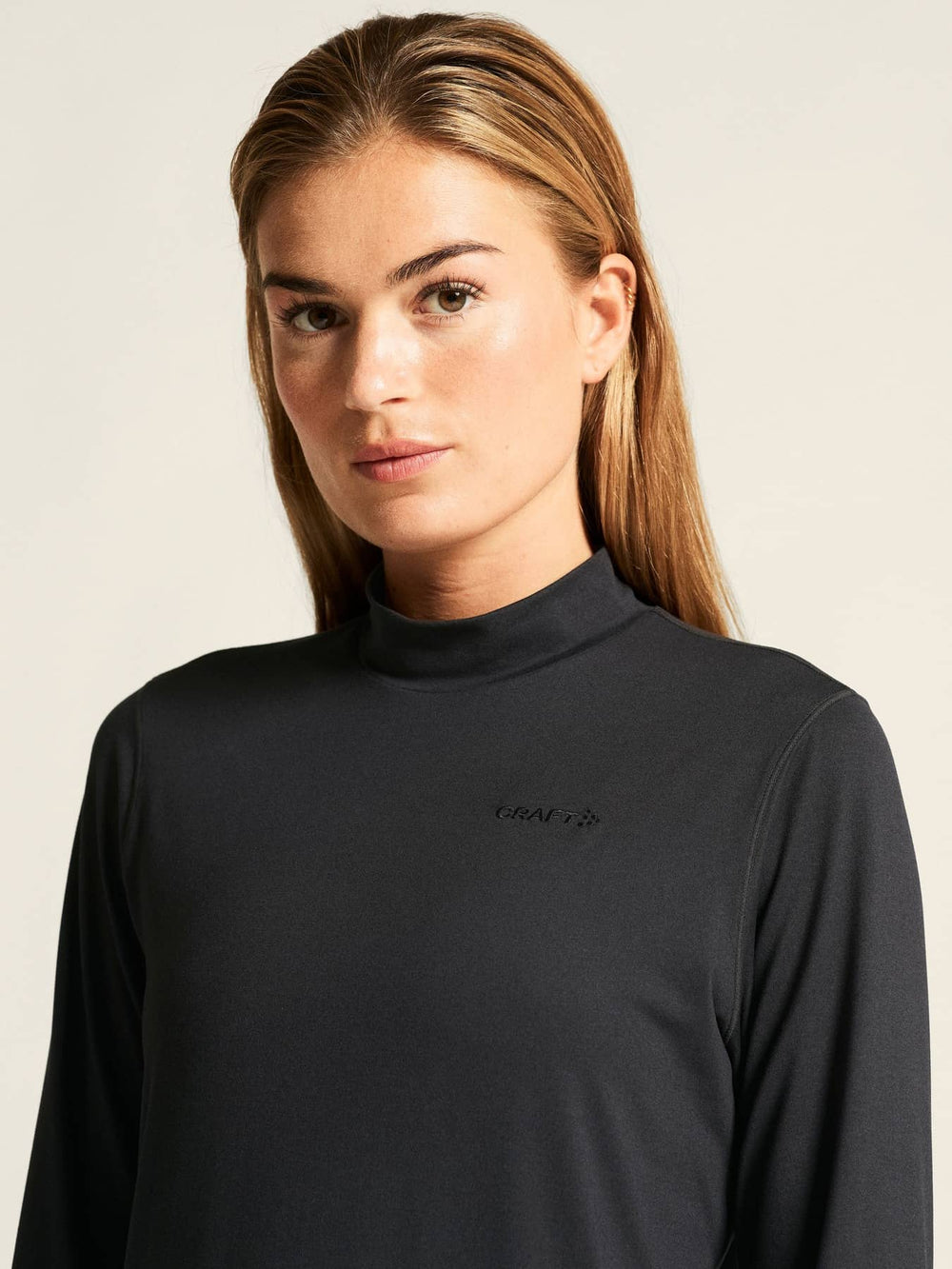Woman wearing a black long-sleeve top with a logo on a beige background