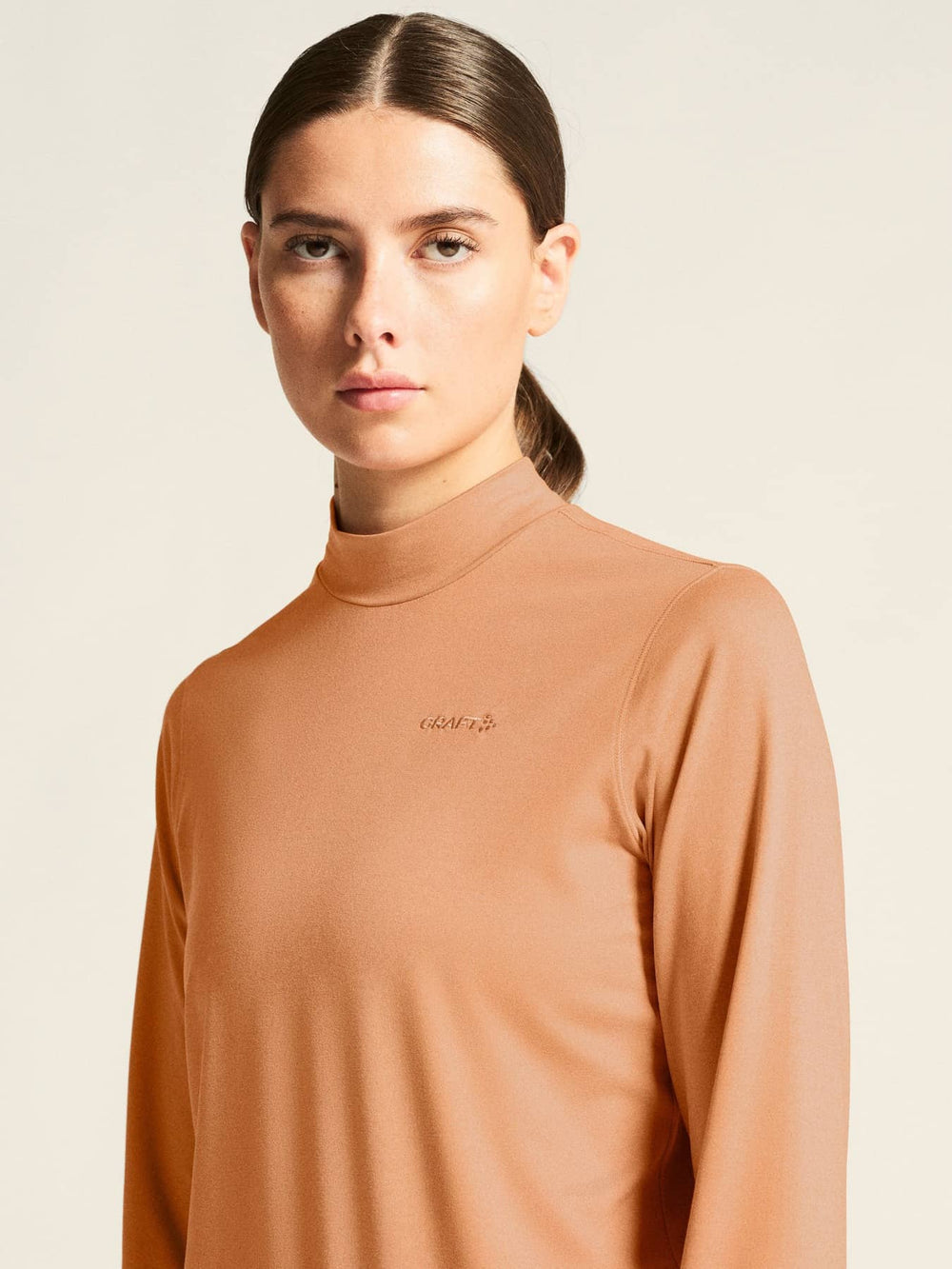 Woman wearing a brown long-sleeve top with a logo on a beige background