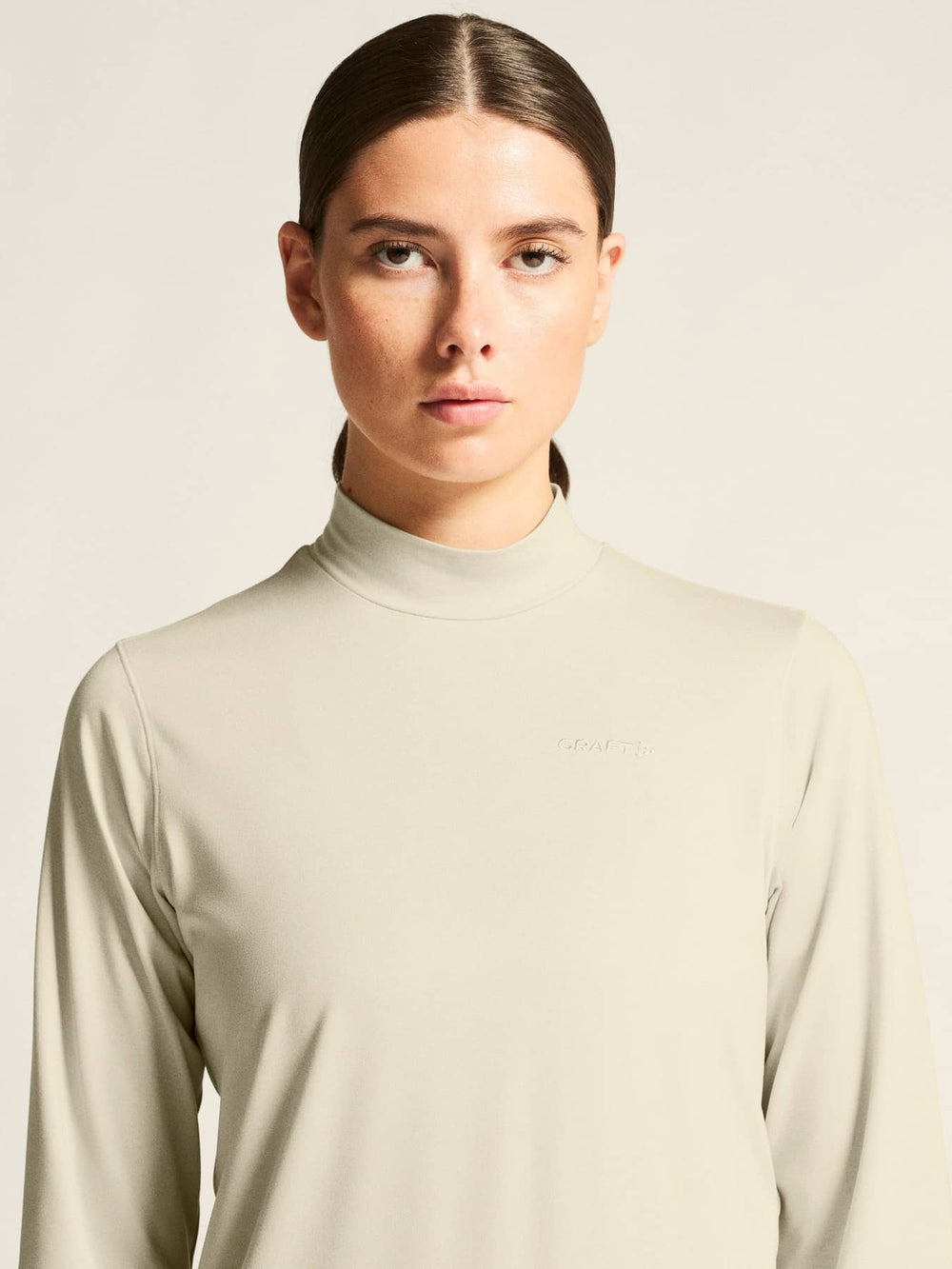 Woman wearing a beige long-sleeve top against a plain background