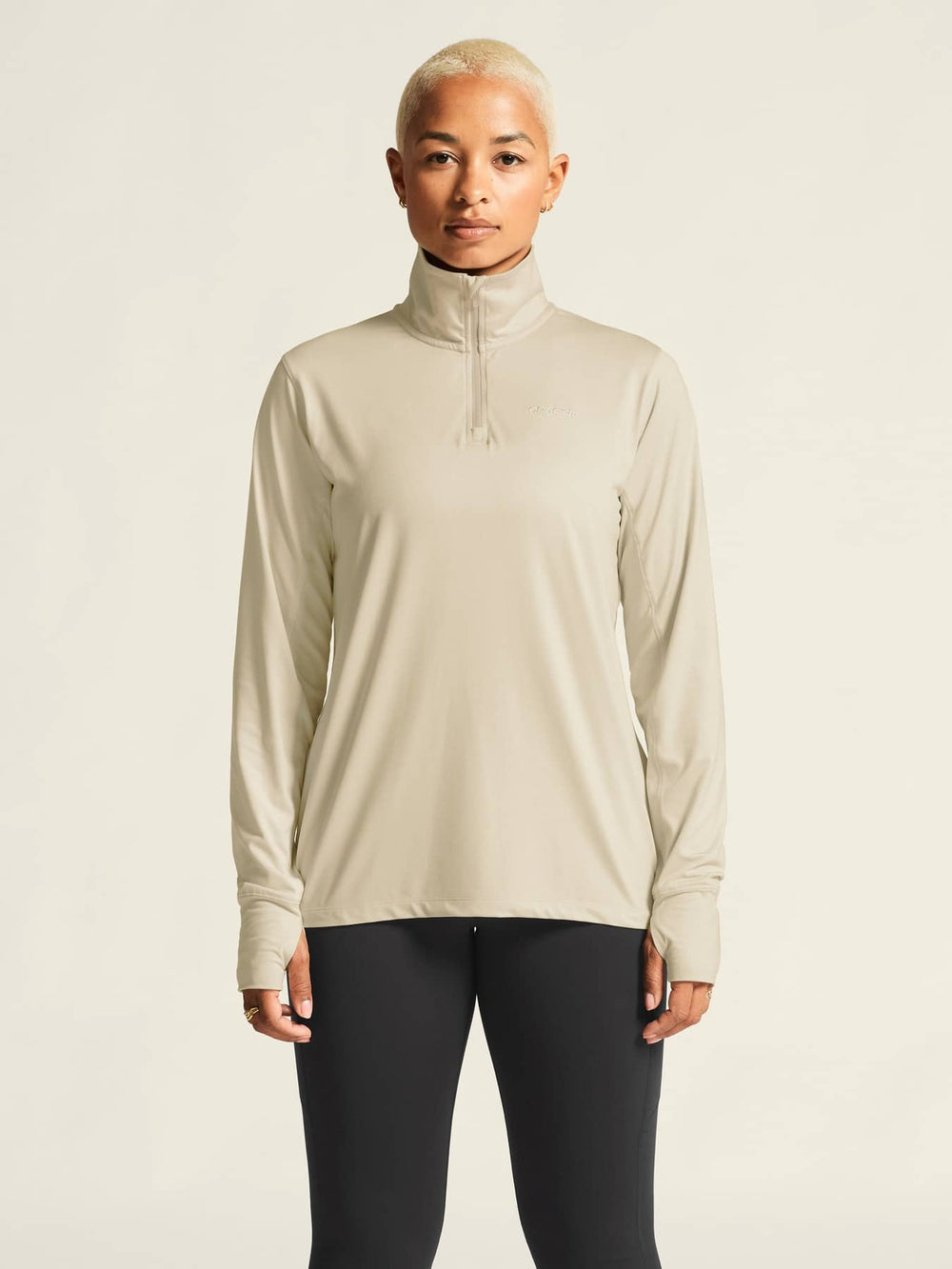 Person wearing a beige long-sleeve athletic top with a zipper on a plain background