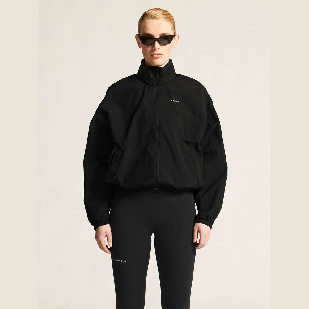 Person wearing a black jacket and pants with a brand logo on a beige background