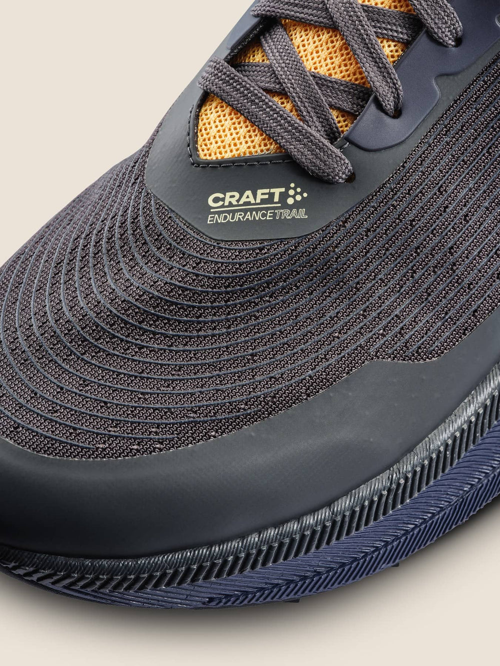 Close-up of a gray and yellow athletic shoe with 'Craft' branding on a beige background