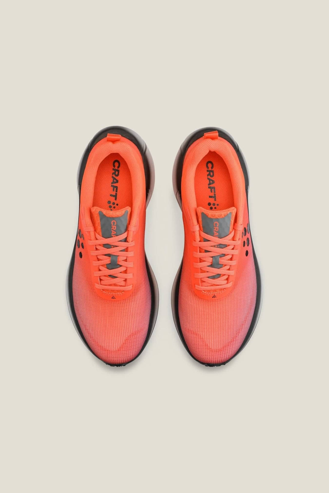 Pair of bright orange running shoes with black soles on a beige background