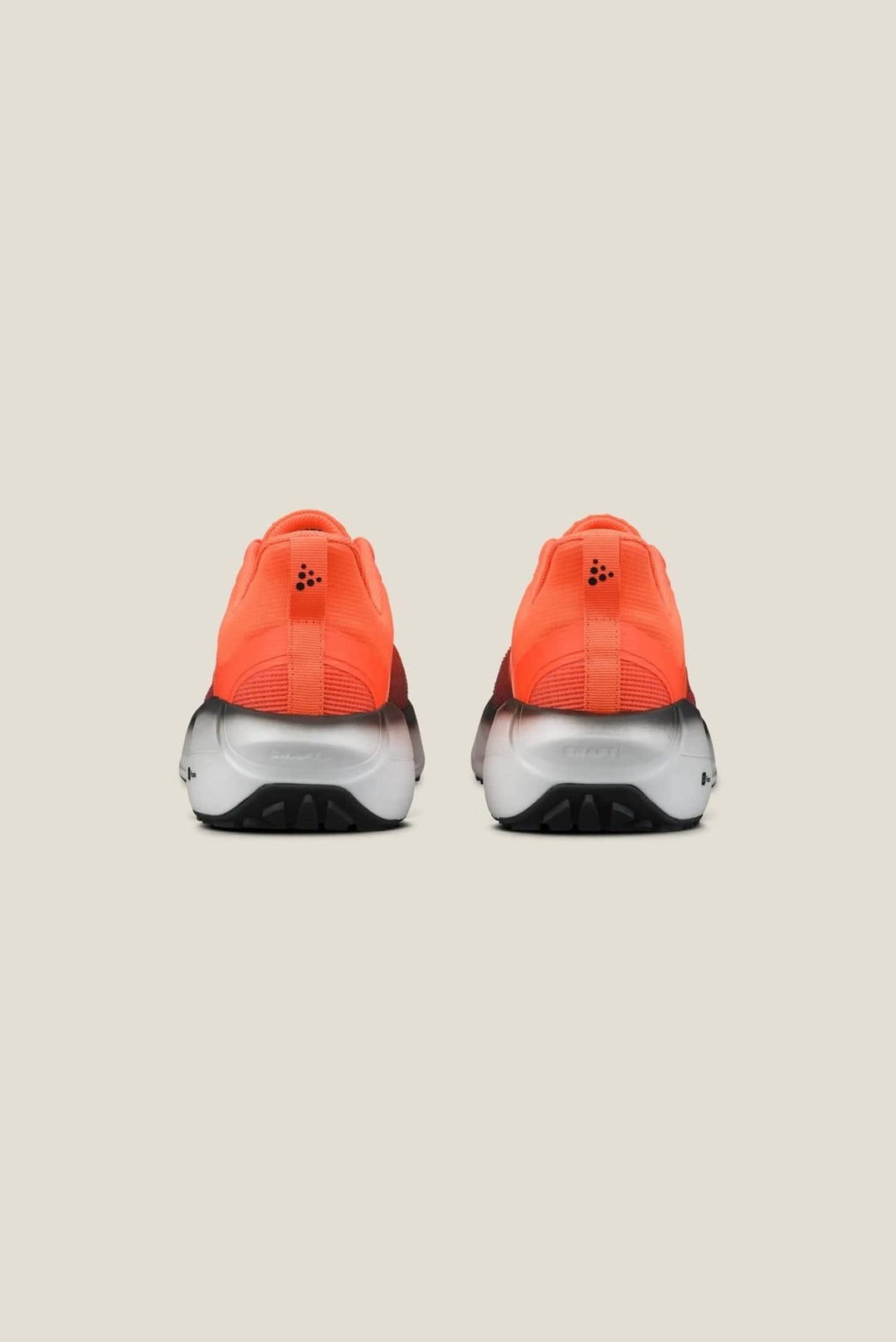 Pair of orange athletic shoes with black soles on a beige background