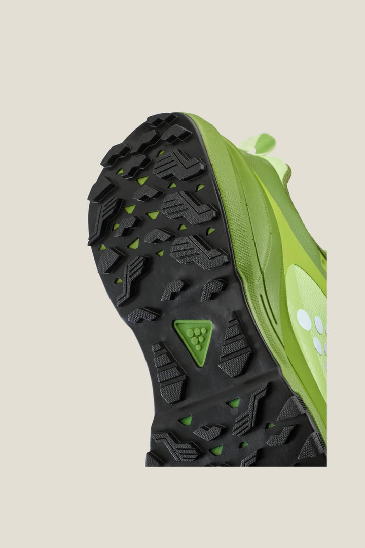 Close-up of a green and black athletic shoe with tread pattern on a beige background