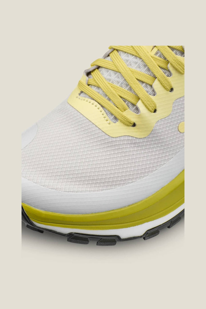 White sneaker with yellow laces and sole on a beige background