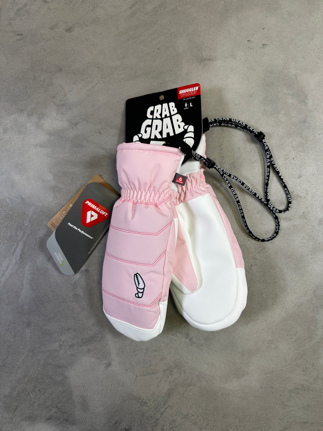Pink mittens with a white sneaker on a gray concrete surface, featuring Crab Grab branding.