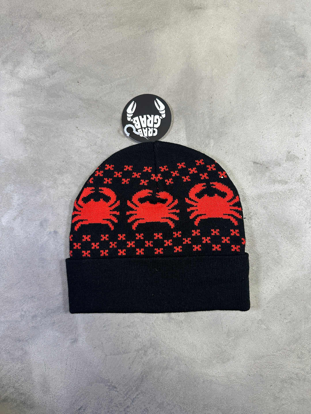 Black beanie with red scorpion pattern on a gray surface