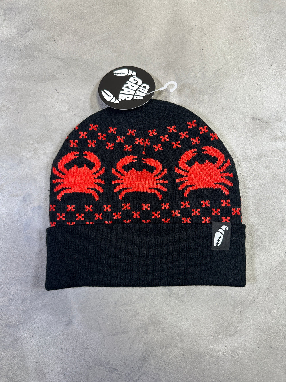 Black beanie with red spider pattern on a gray surface