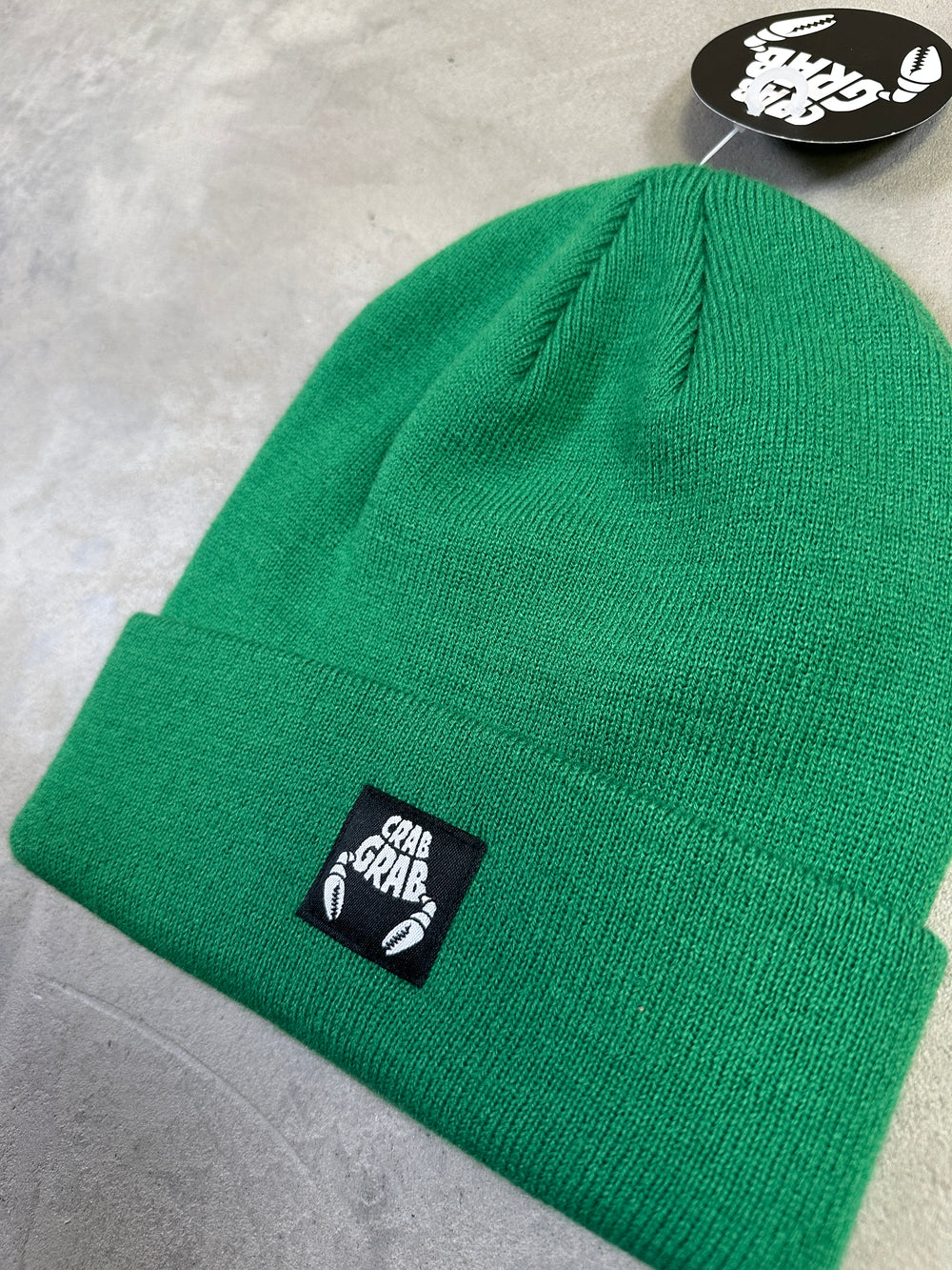 Green beanie with a brand logo on a gray surface