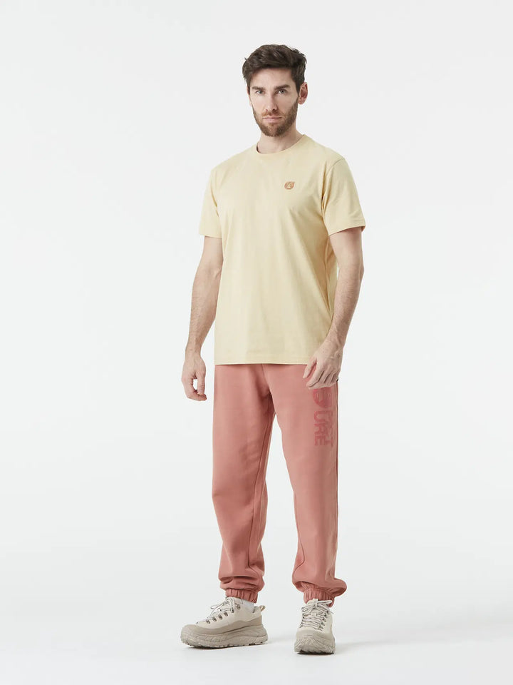 Man wearing a light yellow t-shirt and pink pants on a white background
