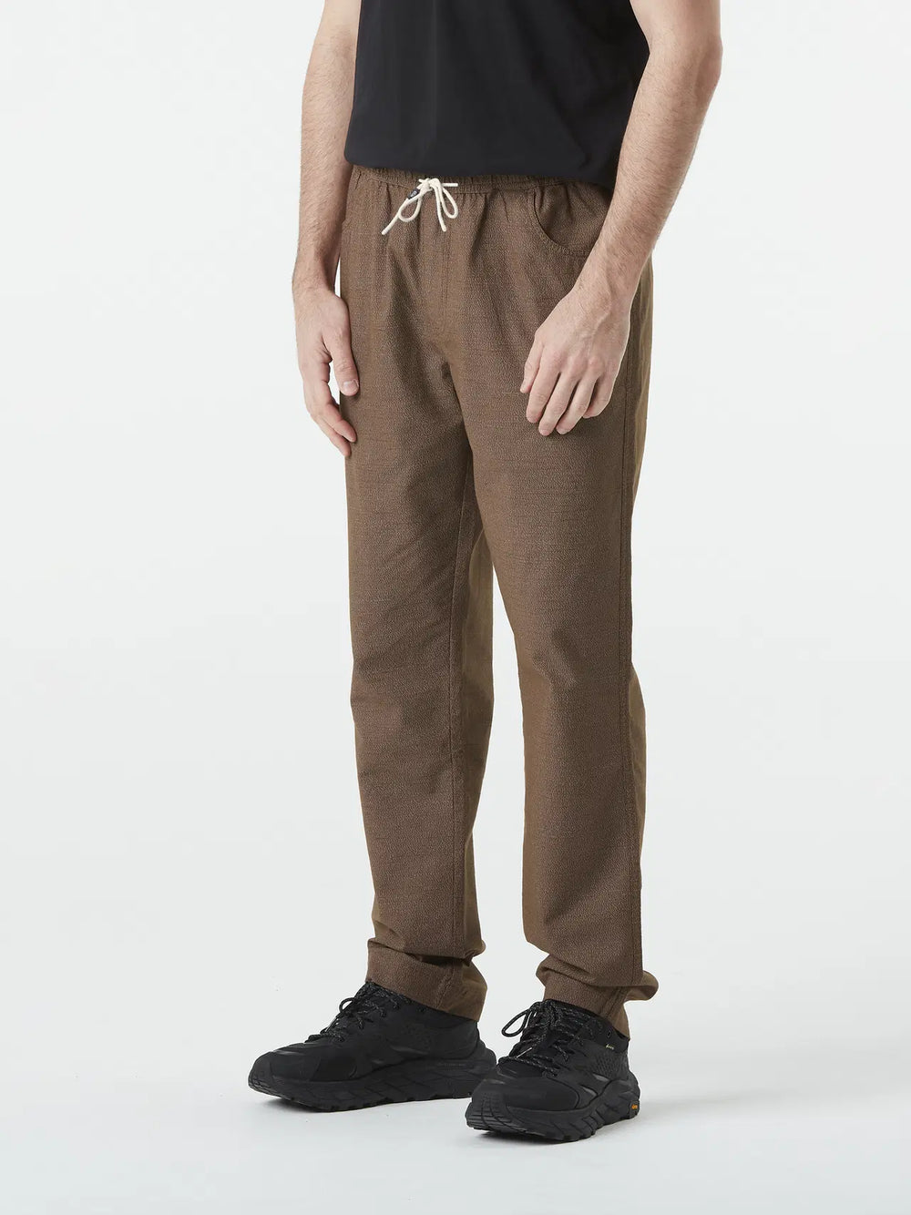 Person wearing brown pants and black shoes on a white background