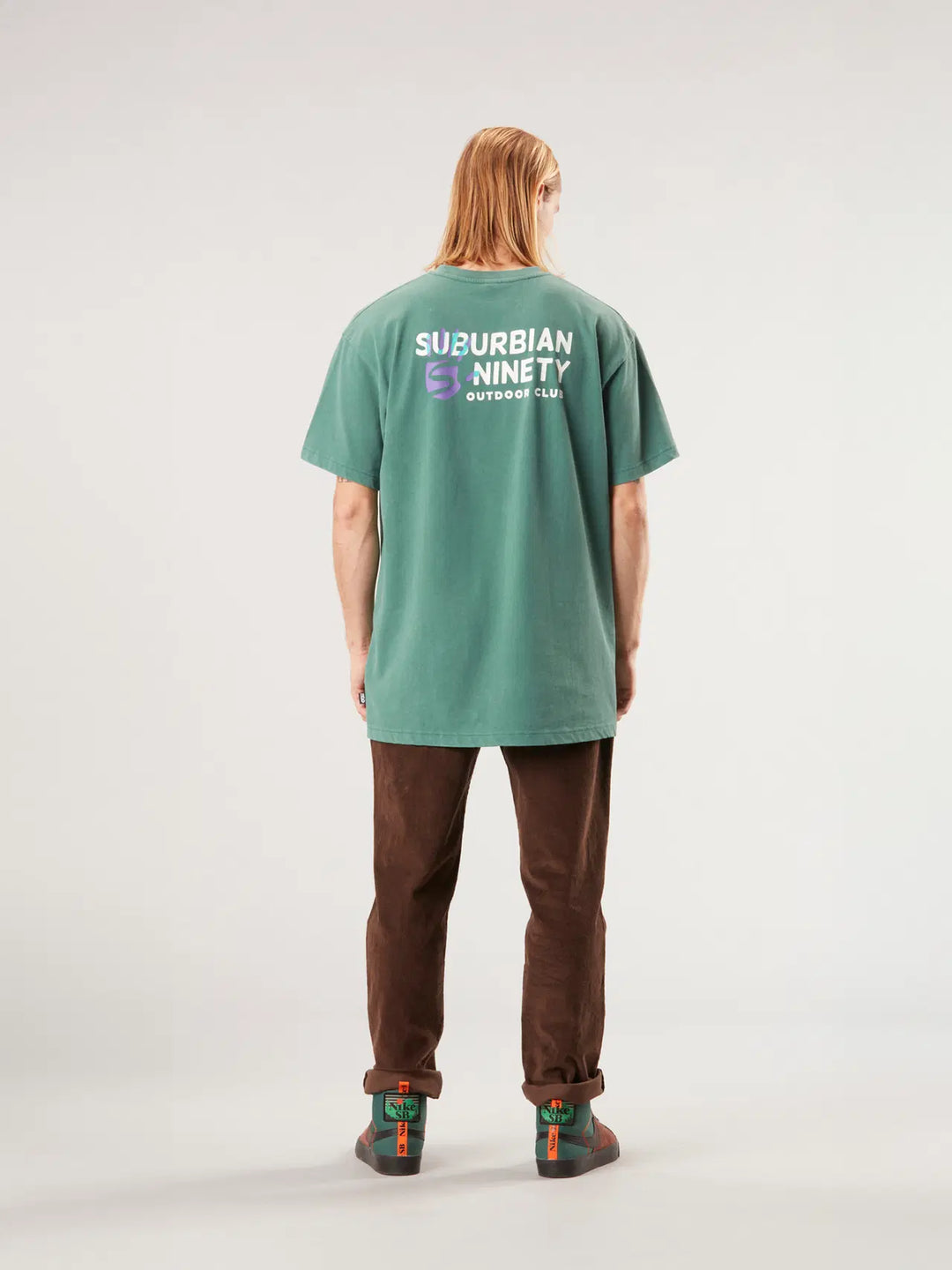 Person wearing a green t-shirt with text on the back, standing against a white background