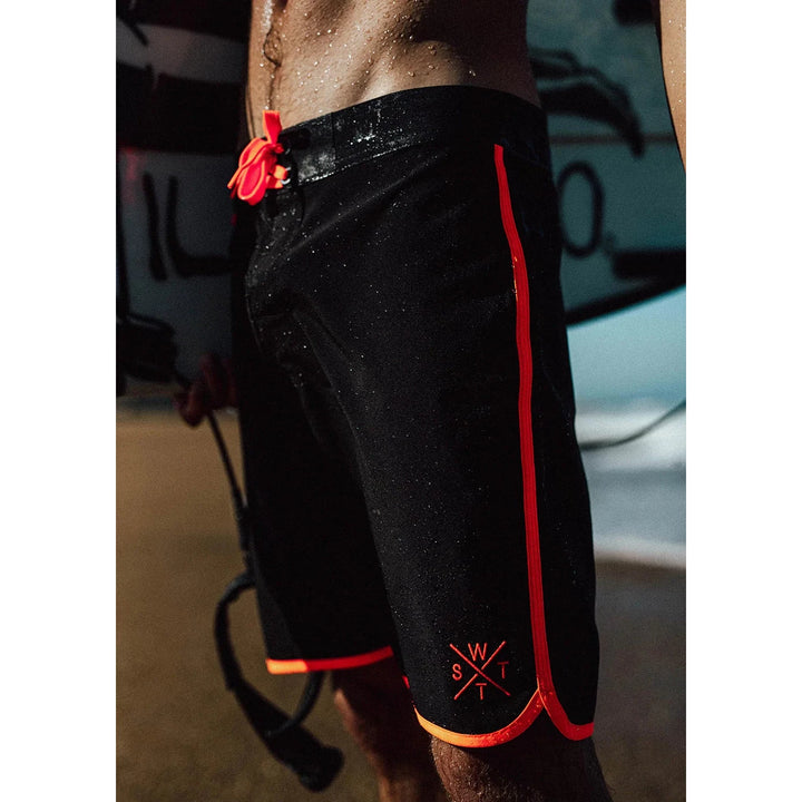 Person wearing black shorts with red accents and a logo, standing in a garage.