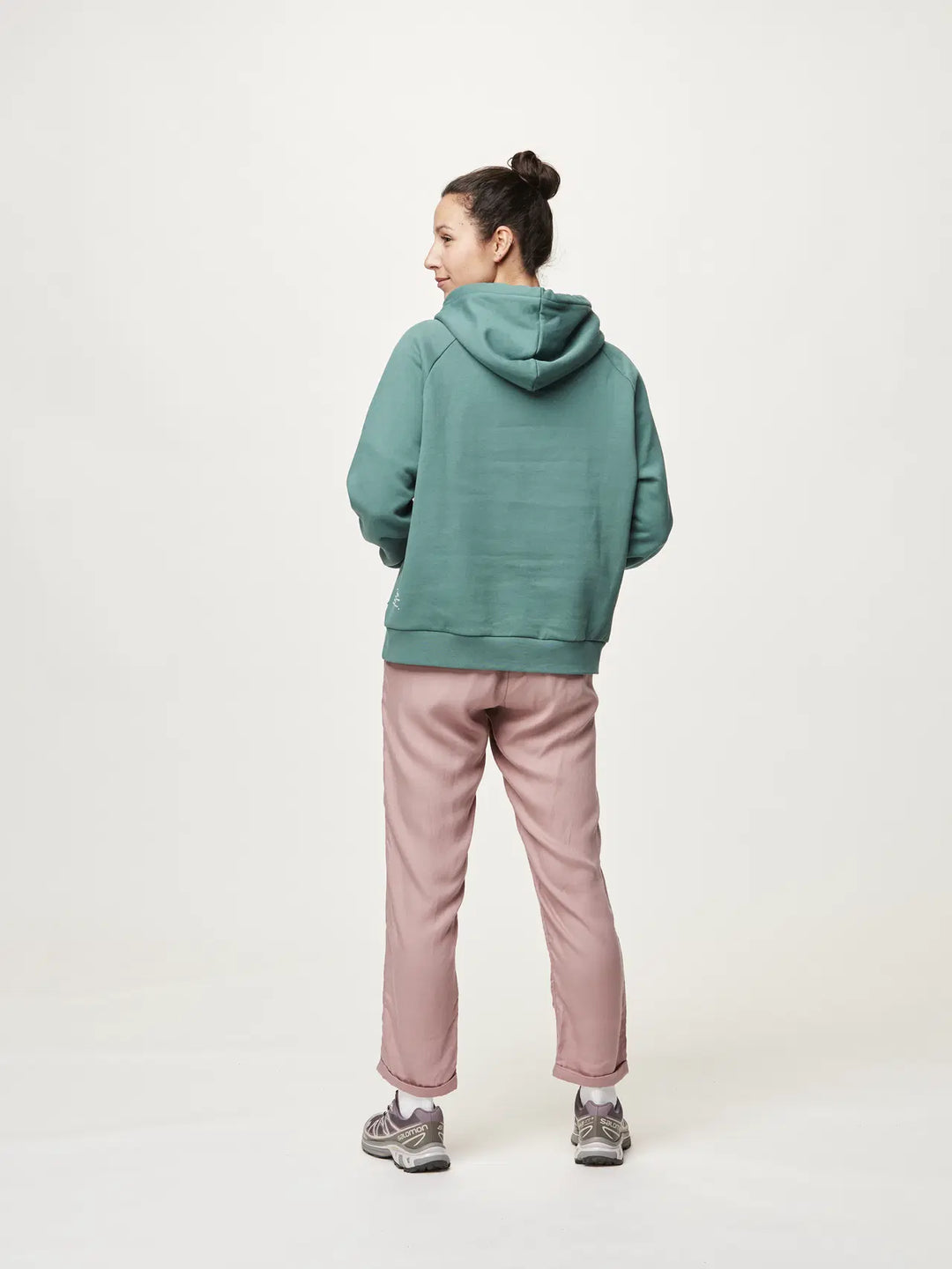 Person wearing a green hoodie and pink pants on a white background